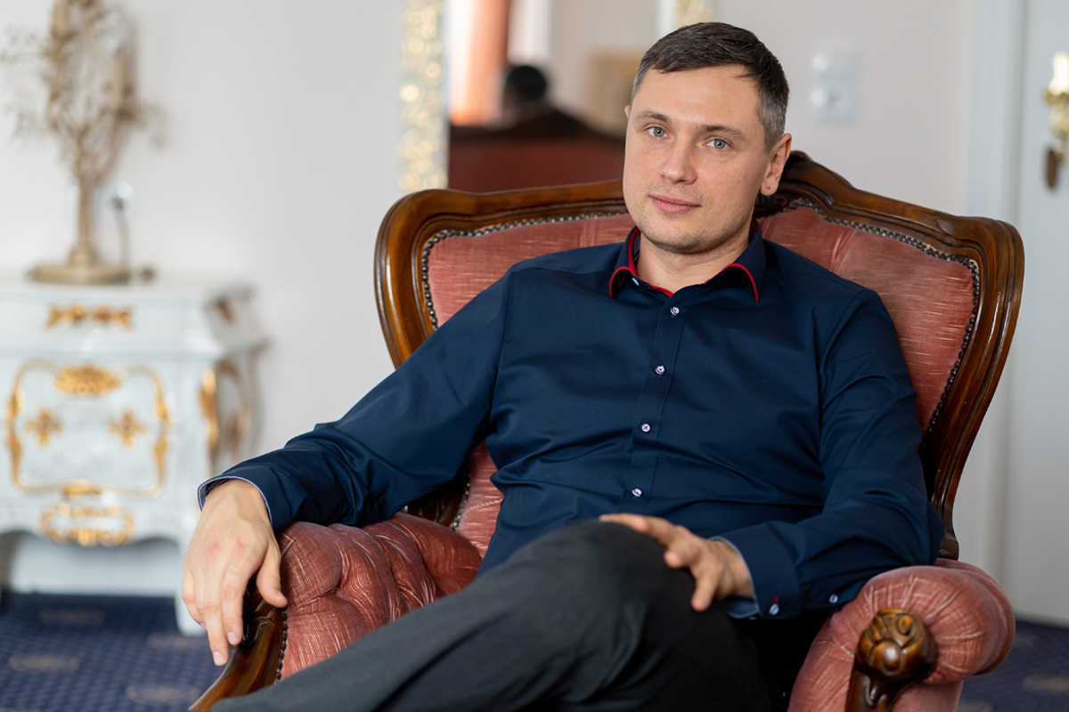 Sergej Metzger, Hochzeitsvideograf und -fotograf, sitzt entspannt in einem altrosa Polstersessel.